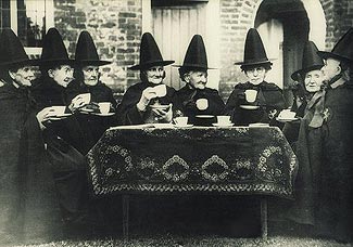 antique photo of a a group of women wearing witche hats and drinking tea